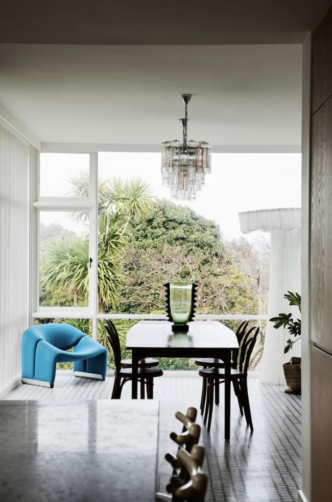 A mid-century modern dining room with emerald coloured chair with a chandelier hanging above in a Melbourne house